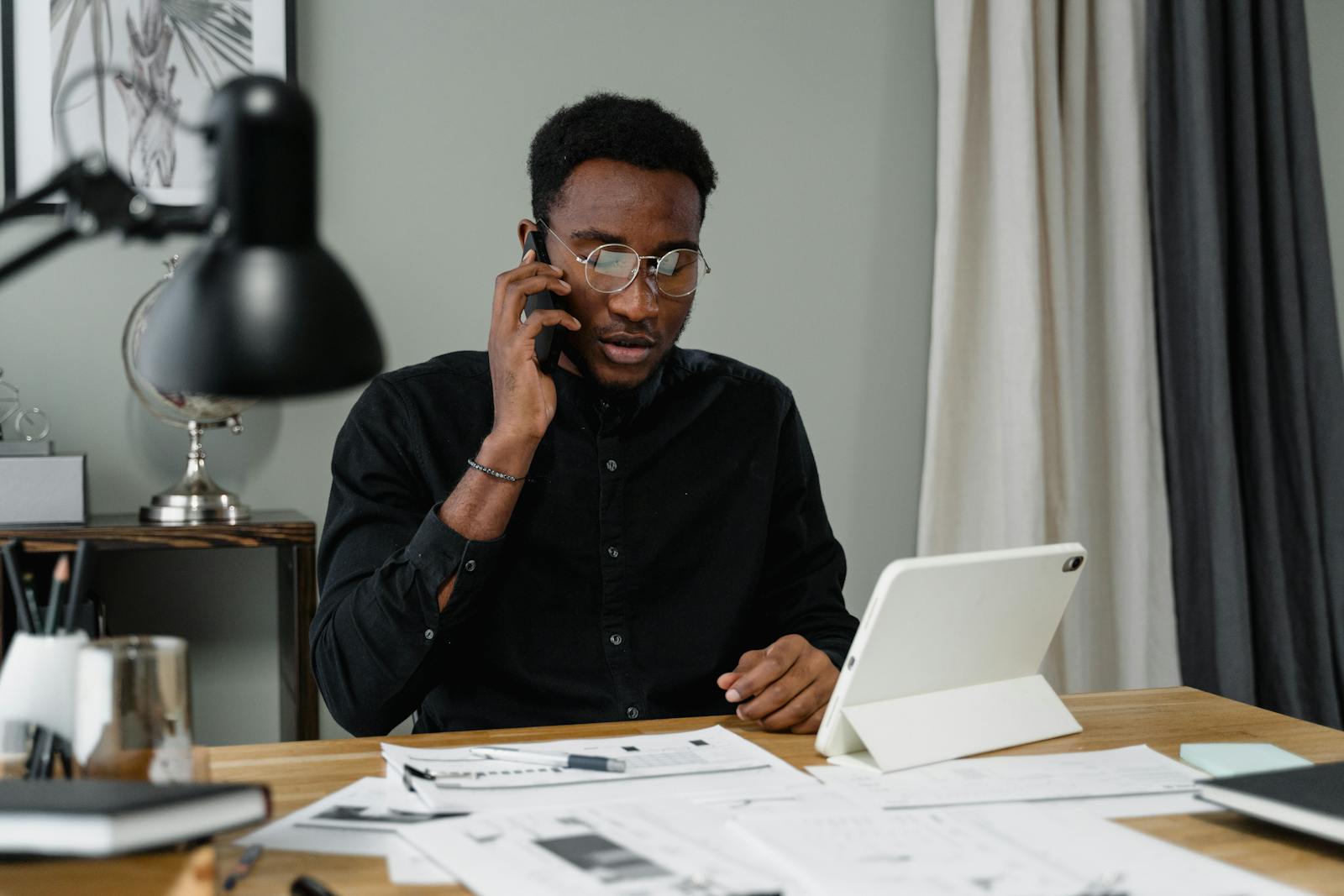 How Long Does It Take to Get VA Disability Benefits? 1 Focused man with eyeglasses making a work-related phone call at his desk with documents and a tablet.