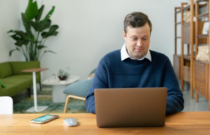 Caucasian man using a laptop in a modern living room setting with plants and shelves.