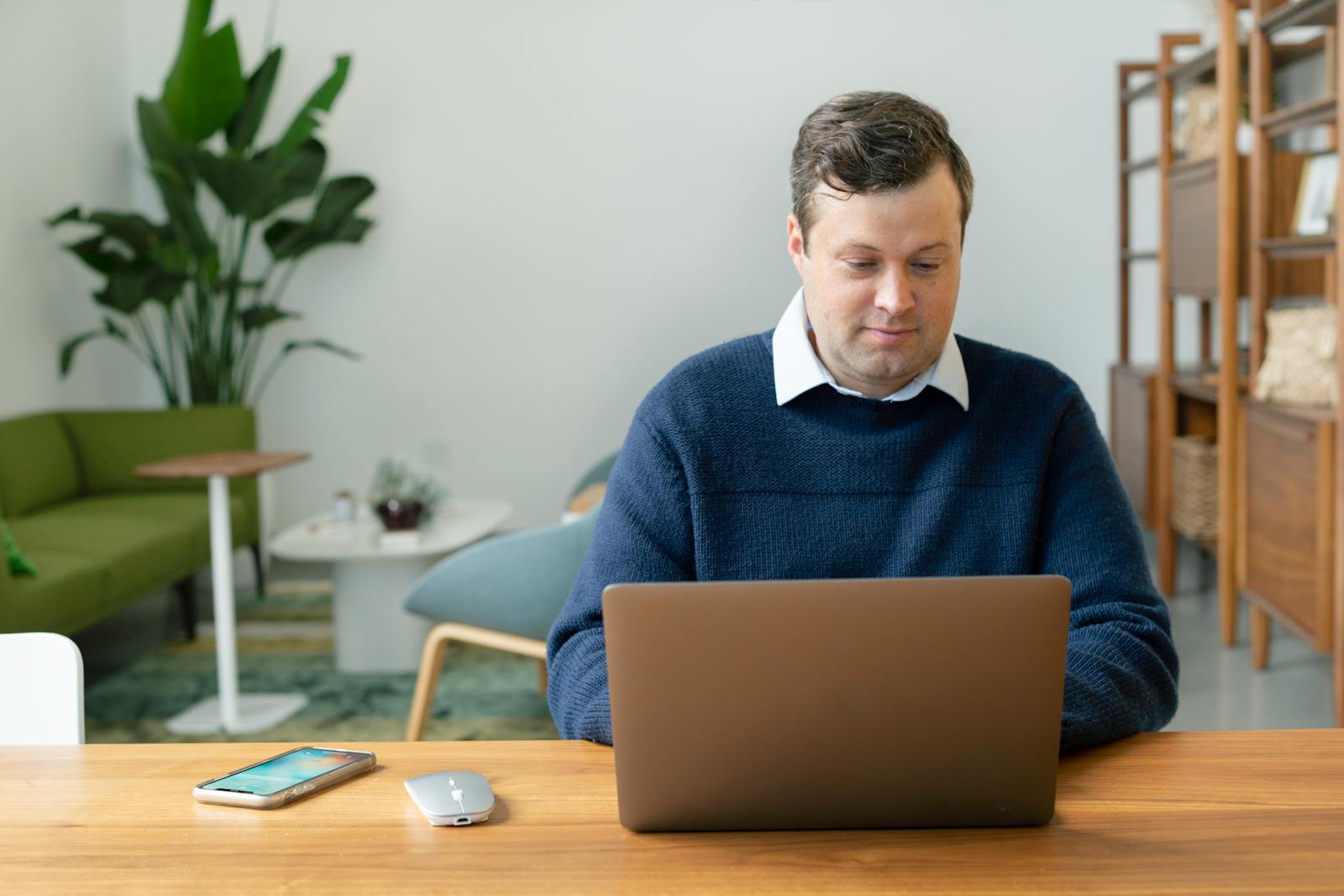 HIPAA Compliance in Social Services Technologies 1 Caucasian man using a laptop in a modern living room setting with plants and shelves.